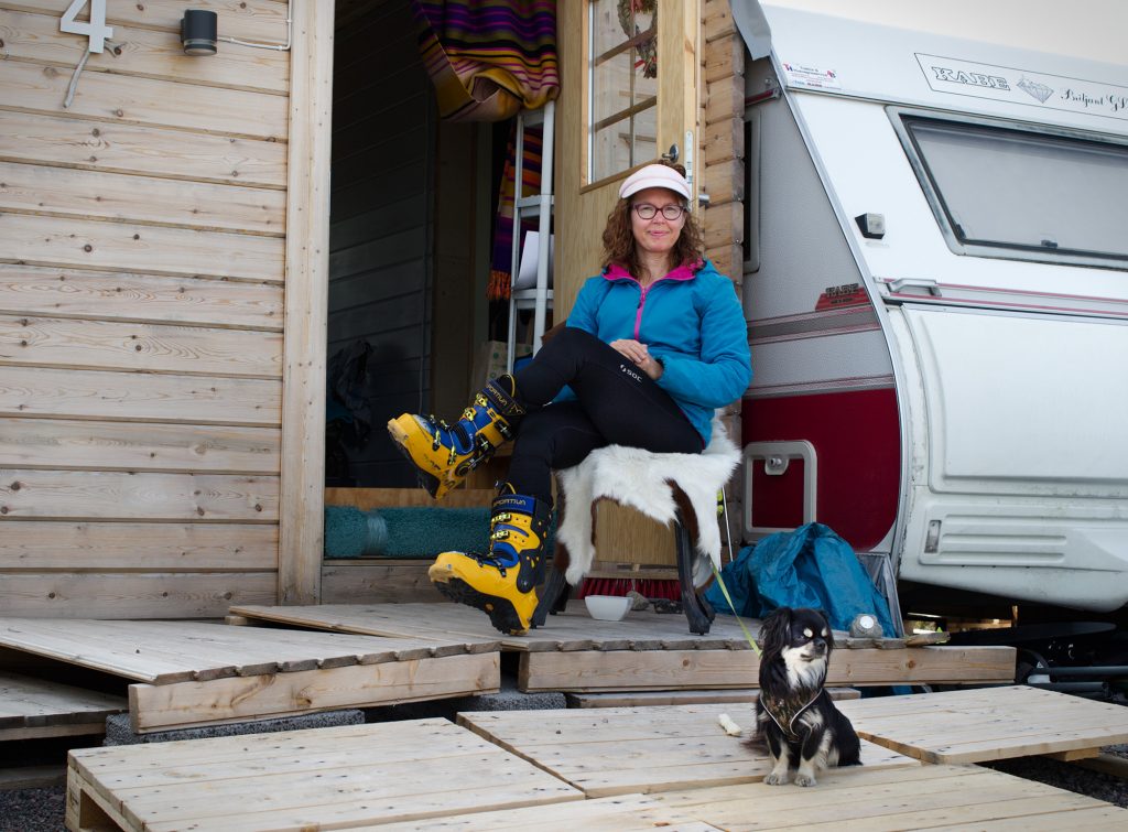 En kvinna sitter med slalompjäxor på benet utanför en stuga.