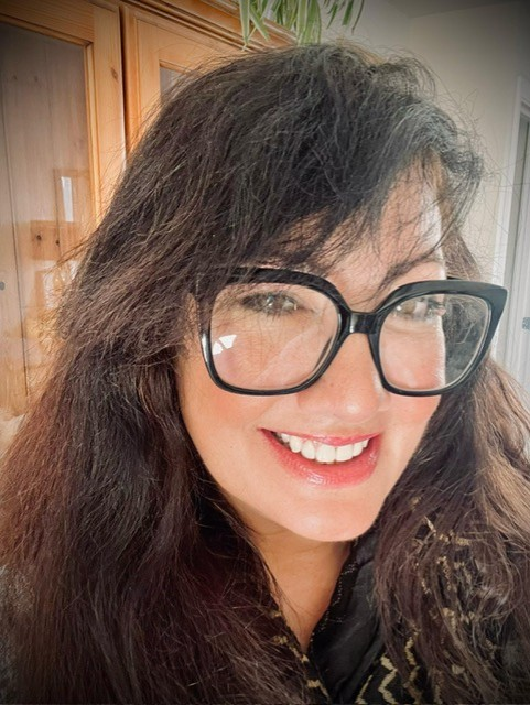 Zaina Gadema watching right into camera, smiling. She is having big glasses with black frame. 