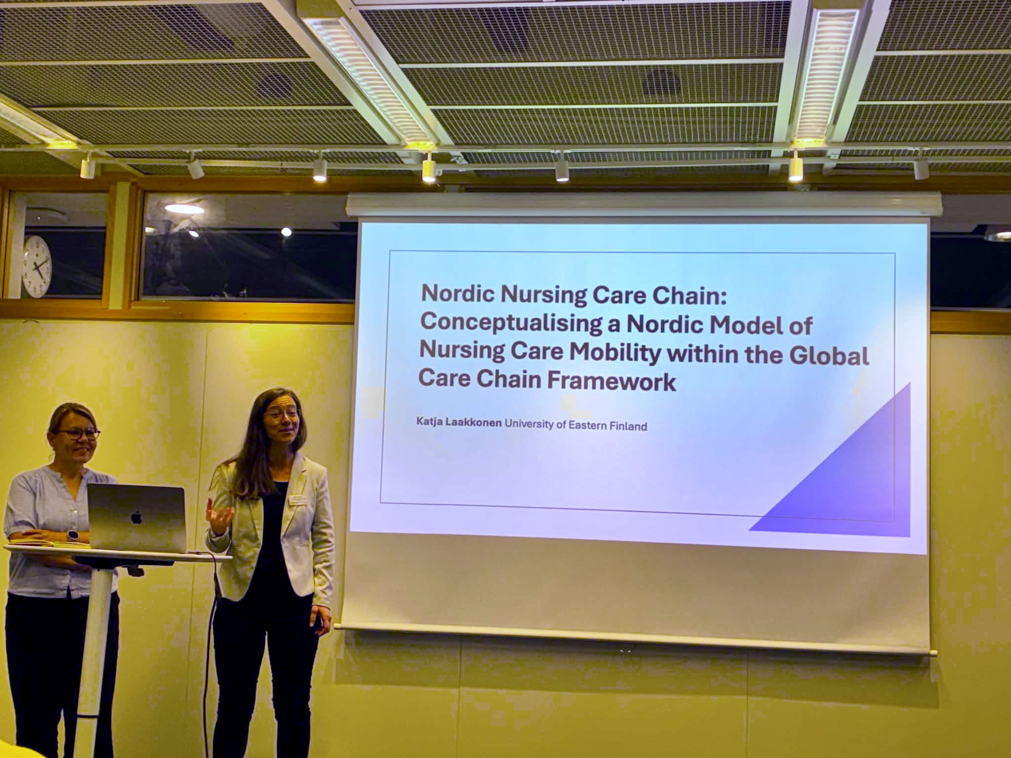Katja Laakkonen and Mariya Bikova standing in front of a screen that has a text 