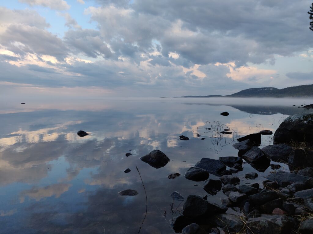 Kuvassa järvi, johon heijastuu pilvet. Järven pinnalla paikoitellen sumua.